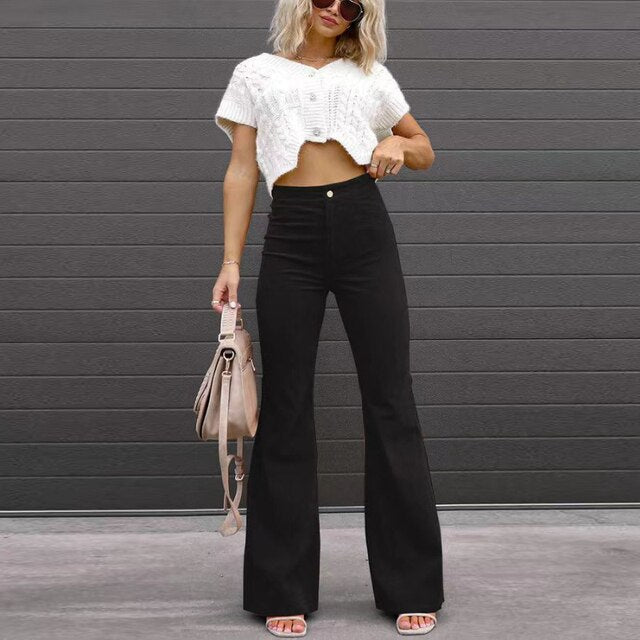 Vrouw in zwarte flared broek en witte crop top, met beige handtas, tegen grijze achtergrond. Modieuze dameskleding, casual stijl.