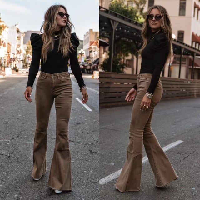 Vrouw in bruine flared jeans en zwarte top, poseert op straat. Modieuze outfit, casual stijl, stedelijke achtergrond, trendy zonnebril.