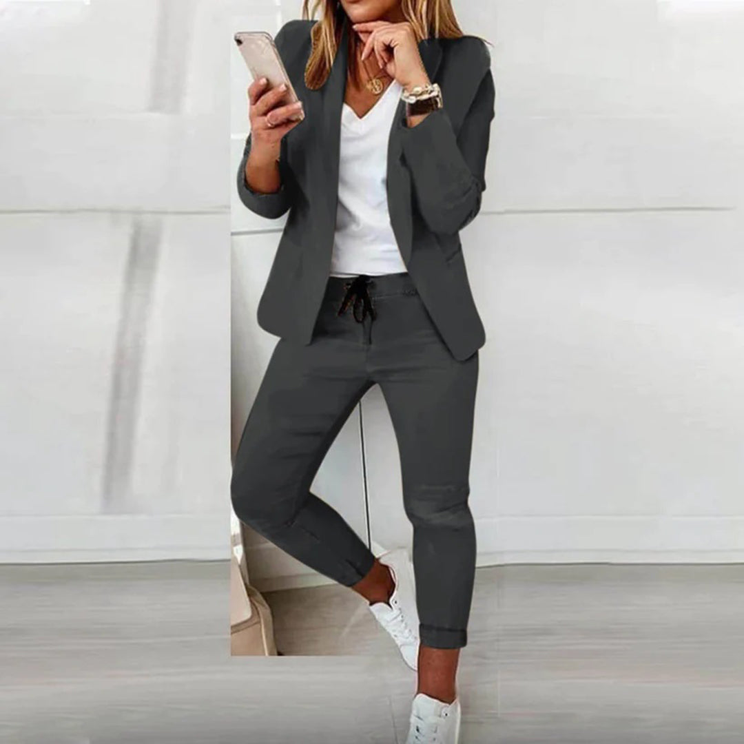 Elegante vrouw in grijs damespak met witte sneakers en smartphone, moderne zakelijke outfit, stijlvolle damesmode, casual chic look.
